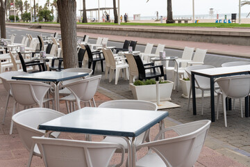 Empty tables and chairs, on a gray afternoon in late summer, on the touristy beach of Gandia. End of summer concept.