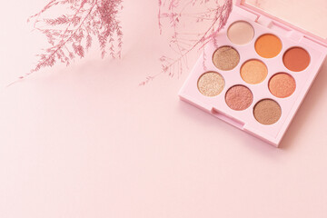Palette of shadows and plants frame. Pink background. Space for text. Concept of makeup and makeup artist