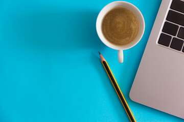 Laptop with coffee cup and pencil on blue background. Home office concept. Top view. Flat lay. Copy space.