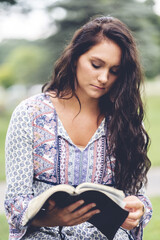 Vertical shot of a Caucasian woman reading a bible at a park