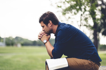 Shallow focus of a male Caucasian praying earnestly at a park in grayscale