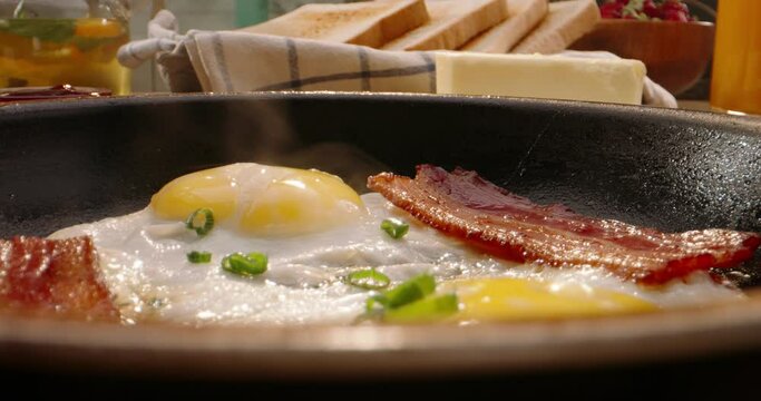 Putting frying pan with freshly fried eggs and bacon on table with served nourishing balanced breakfast - morning meal preparation 4k footage