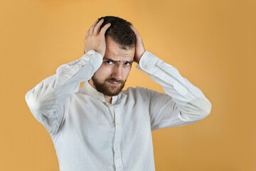 A young man with a beard with suffering on his face holding his head, he had a hard day's work with stress, now he has a headache