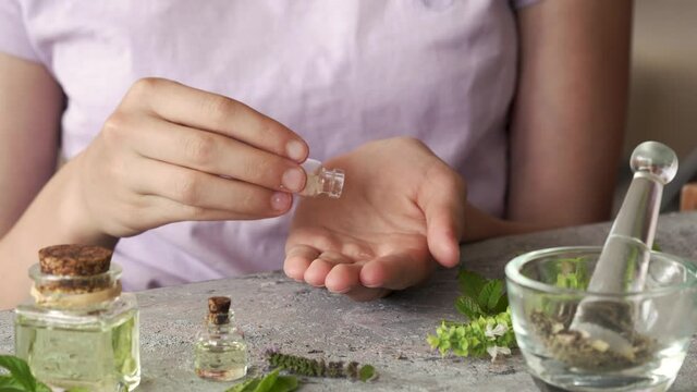 Teenage girl's hands taking homeopathic pills or globules from a glass bottle, with essential oils and herbs in the foreground