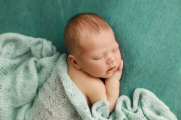 Sleeping newborn baby on a green background covered by blanket. A few days from birth. Hand under the cheek, Photoshoot for the newborn. 