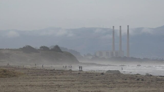 Morro Bay smokestacks or stacks in distance with people walking on beach.