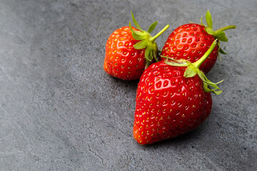 Three red ripe strawberries over dark