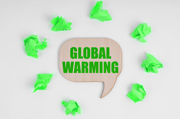 On a white background, there are crumpled green pieces of paper and a wooden sign with the inscription - Global Warming