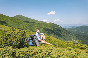 mountain hiking concept. a guy with a big backpack squatting to rest. hiker on top of a mountain