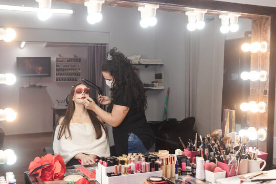 Makeup artist finishing details of a Dia de Los Muertos makeup for a beautiful girl in the beauty salon.