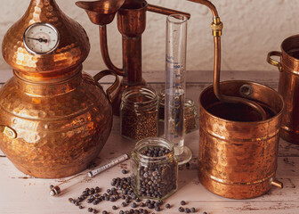 Alambique de cobre utilizado para destilar con botánicos, enebro, cardamomo y accesorios sobre una mesa de madera. - obrazy, fototapety, plakaty