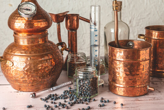 Alambique de cobre utilizado para destilar con bot&aacute;nicos, enebro, cardamomo y accesorios sobre una mesa de madera.