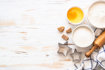 Baking ingredients. Flour, sugar, egg and rolling pin at white wooden table. Top view with copy space.