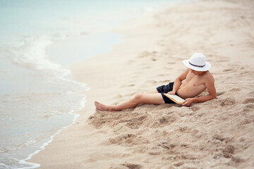 A teenager reads a book on the beach. 