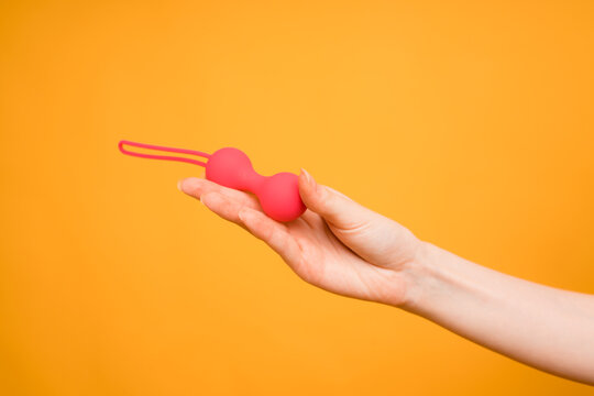 A woman's hand holds red Kegel balls on an orange background.Useful for a sex shop