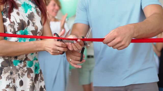 Man and Woman Cut the Red Ribbon in Honor of the Opening of a New Store, While Many Unrecognizable People are Applauding in the background. Married Couple Opens Their Own Business. Slow motion.
