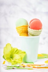 Wafer cup for ice cream with macarons and green gladiolus on a light marble background