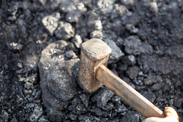 A man smashes large pieces of coal with a sledgehammer. Mineral solid fuel for stoves and fireplaces in the cool season.