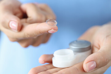 Woman holds contact lens and storage container on finger closeup