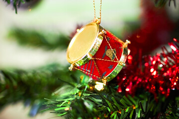 Christmas tree drum decoration hanging on branch with red tinsel closeup