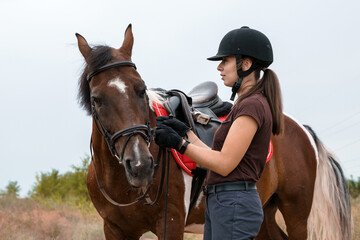 A girl in a field stands next to her skewbald horse