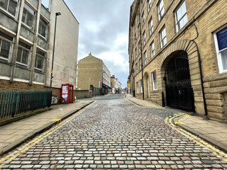 View along, Duke Street, with Victorian stone cobbles, buildings, and a cloudy sky in, Bradford, Yorkshire, UK