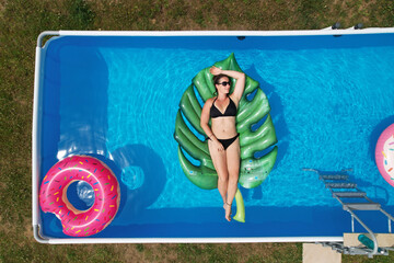 TOP DOWN: Female in a bikini relaxes in her garden pool on a sunny weekend.