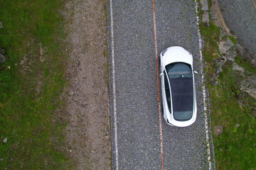 TOP DOWN: Modern white car cruises along empty cobblestone road in Switzerland.