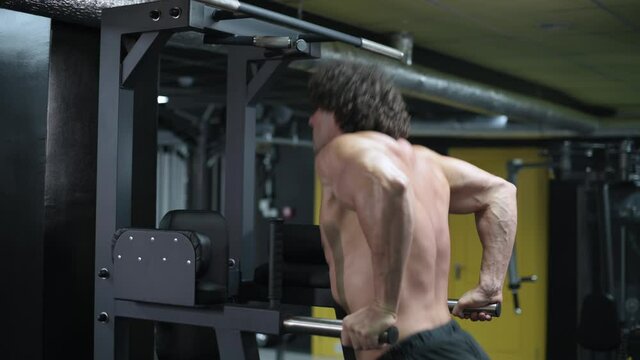 Man exercising on parallel bars. Young athlete exercising in gym. Steadicam shot, side view.