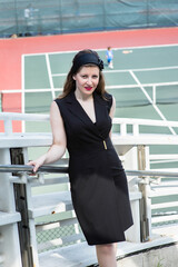 Dressing in black sleeveless clothes, a beautiful woman is standing by a tennis court and relaxing.