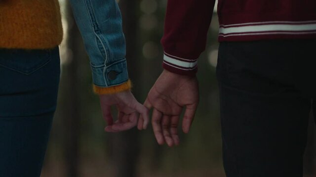 teenage couple holding hands in forest at sunset boyfriend playfully holds girlfriends pinky finger sharing romantic connection in woods happy young lovers