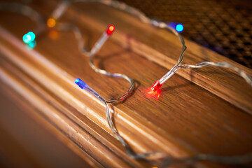 Closeup of multi coloured christmas fairy lights on a warm wooden shelf with a shallow depth of field soft focus bokeh 