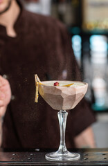 male bartender sprinkles on glass with cold cocktail decorated with dried pineapple.