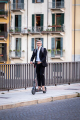 Handsome businessman in suit riding an electric scooter while commuting to work in the city. Ecological transport concept