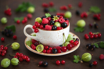 Berry mix in a mug. Cherries, raspberries, gooseberries and red currants on a brown background. Berry still life.