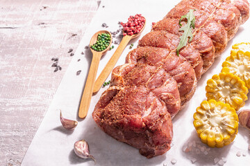 A piece of raw pork loin, marinated fresh meat tied with culinary twine, sweet corn and spices