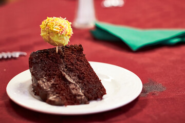 Slice of chocolate fudge cake garnished with cake pop being eaten with a spoon on a red tablecloth for christmas