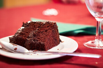 Slice of chocolate fudge cake garnished with cake pop being eaten with a spoon on a red tablecloth for christmas