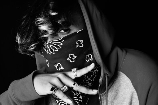 Grayscale Shot Of An Asian Person Wearing A Hoodie And Bandana Showing His Rings