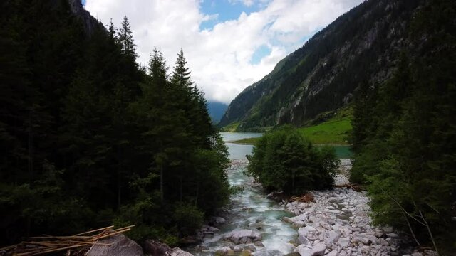 Flug zum Stillup Speichersee im Zillertal in &Ouml;sterreich. Luftaufnahme mit der Drohne. Vom Bach mit B&auml;umen im Vordergrund, zum Stausee mit t&uuml;rkisem Wasser. Aerial drone view of Austria. 