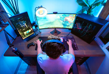young caucasian gamer boy playing in his room gamer with blue and pink leds lights with video game...