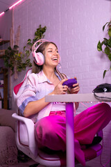 Young caucasian gamer girl playing in her room gamer with pink led lights with video game controller on her winning computer