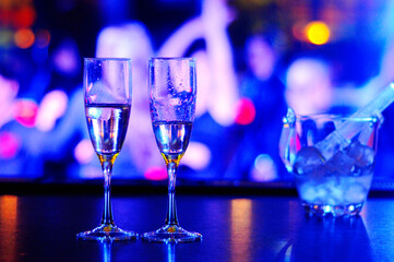 Two glasses of champagne and a bucket with ice are on the table opposite the tanspol in a nightclub