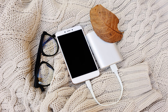 A Composition Of A Smartphone, A Portable Crib, Glasses And A Dry Leaf Of Walnut On A Knitted Background. Autumn Layout
