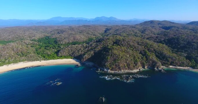 Backward Flying Aerial of Sailboat in a Beach Bay with Small Rocky Islands 