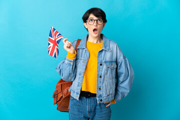 Woman holding an United Kingdom flag over isolated background looking up and with surprised expression