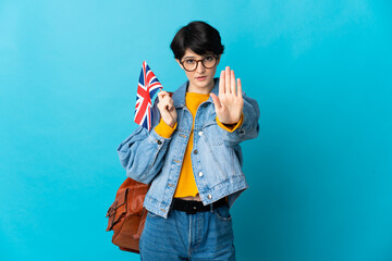 Woman holding an United Kingdom flag over isolated background making stop gesture