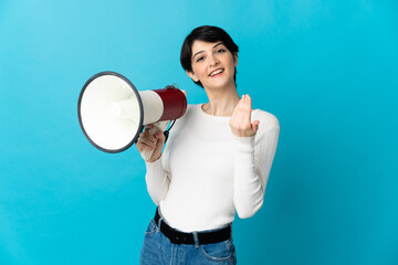 Woman with short hair isolated on blue background holding a megaphone and inviting to come with hand