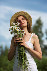 Tender young girl hugs a bouquet of daisies in a field against the backdrop of a stormy sky.