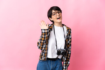 Young photographer woman isolated on pink background saluting with hand with happy expression